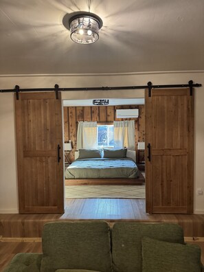 Ein Schlafzimmer mit einem Bett, einem Fenster mit Vorhängen, einer Deckenlampe und Holzwänden.