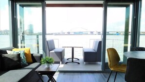 Un interior moderno con sofá, sillas, una mesa y vista a un cuerpo de agua con un puente a lo lejos.