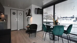 Un interior moderno con zona de comedor, cocina y ventanas amplias con persianas.