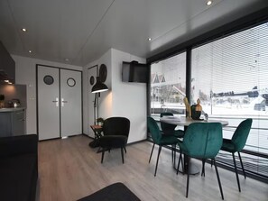Ein modernes Interieur mit Essbereich, Küche und großen Fenstern mit Jalousien.