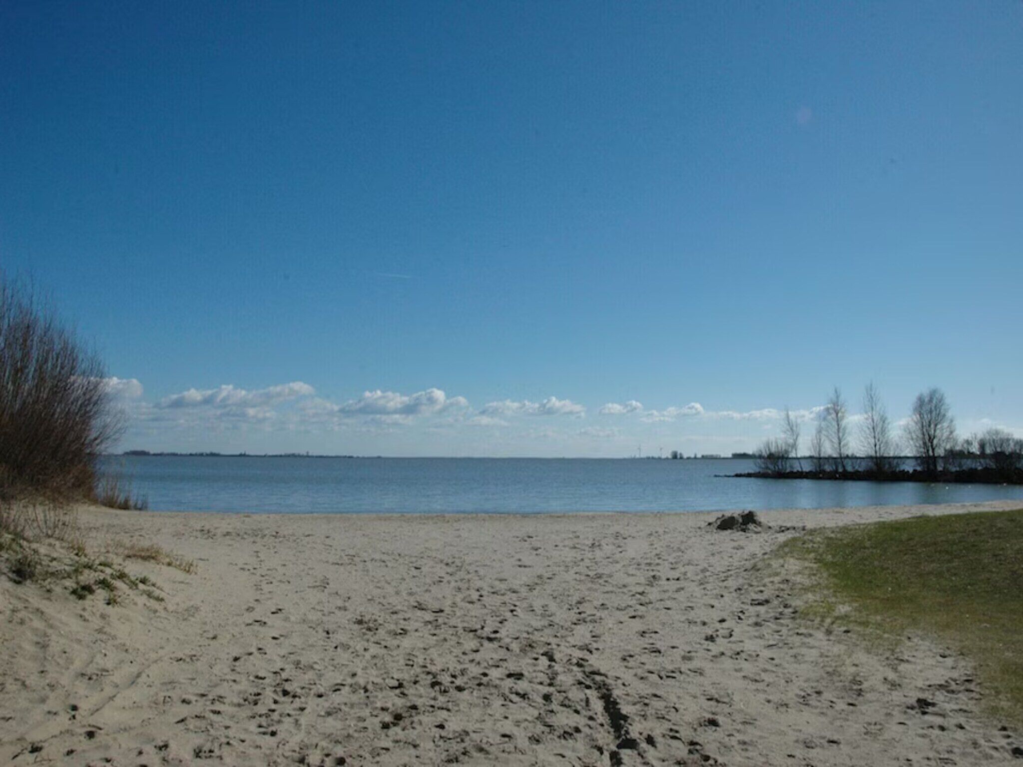 A beach with a clear sky, a sandy shore, and a calm body of water.