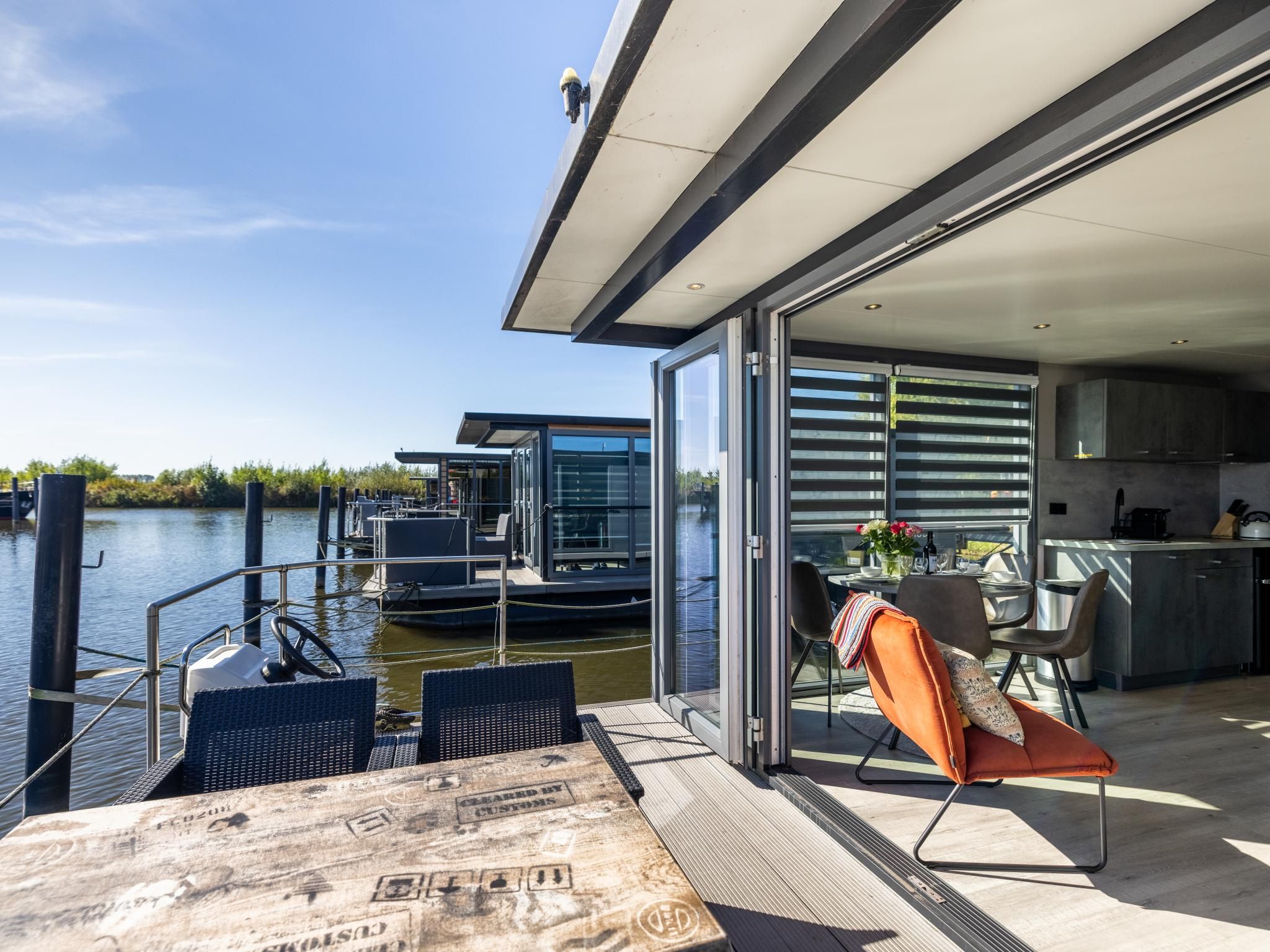 A modern boat with a glass-enclosed dining area, a kitchen, and a view of the water.