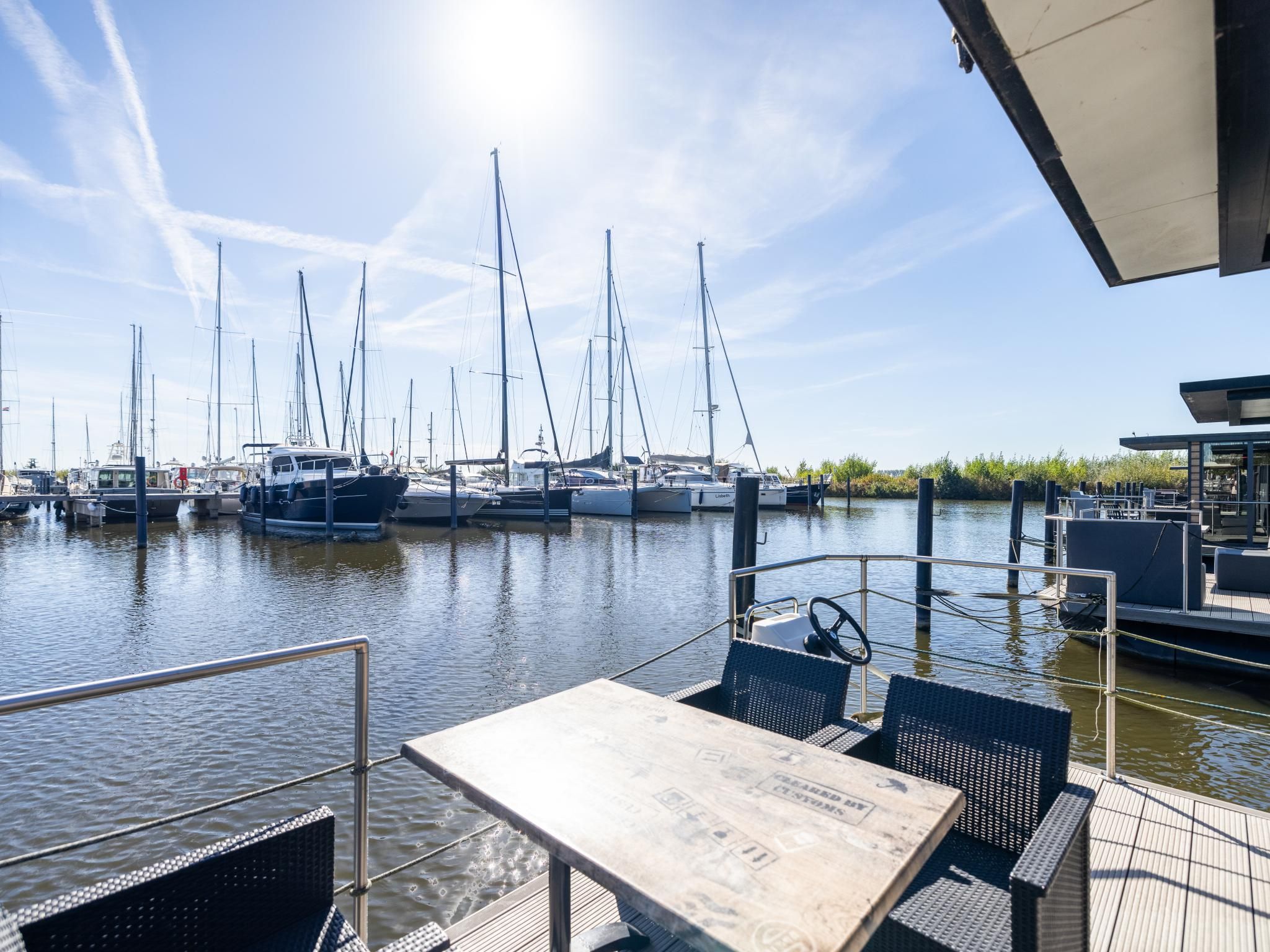 A marina with boats docked, a table and chairs on a wooden deck, and a clear sky.