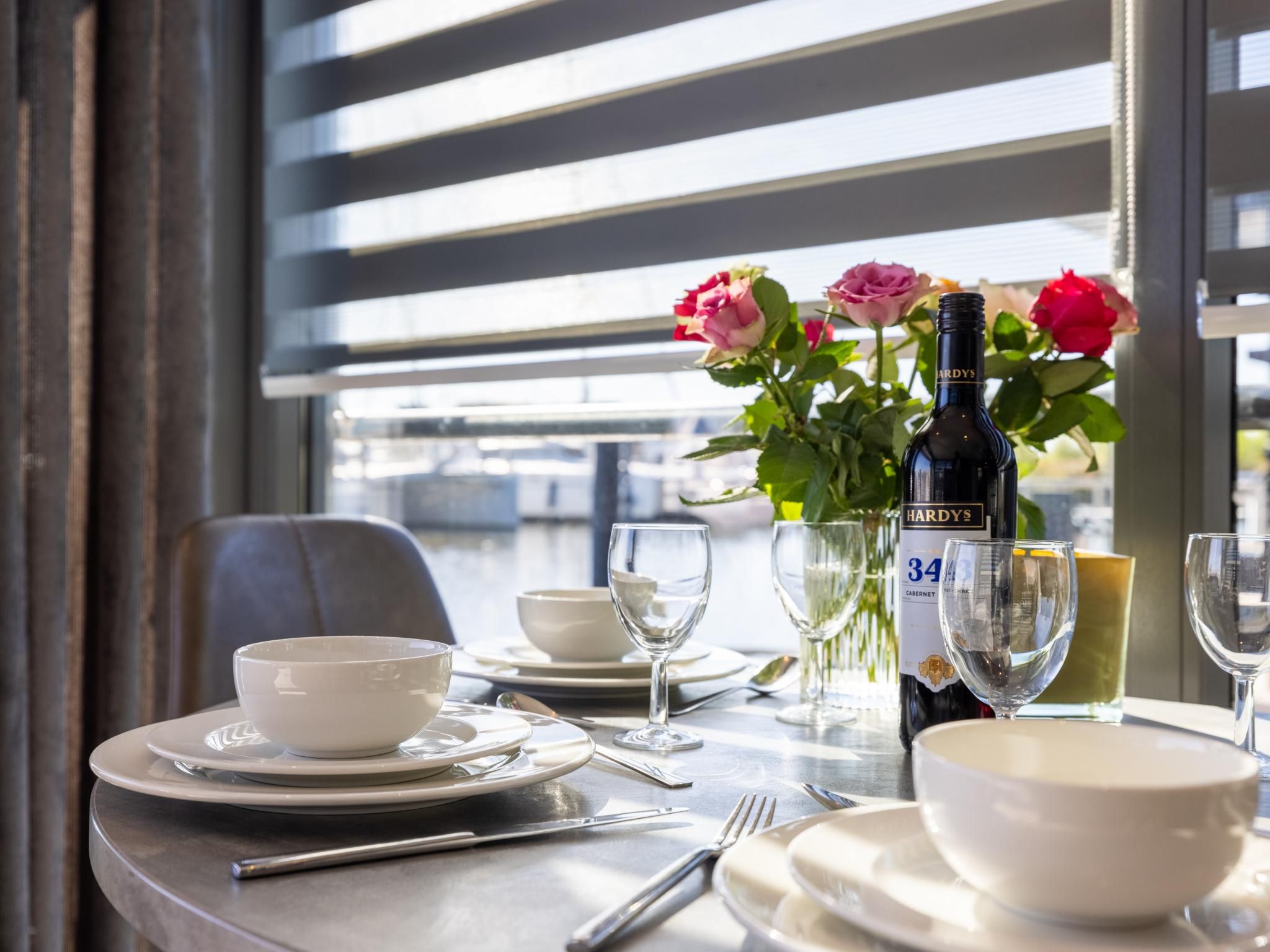 A dining table set with plates, bowls, cutlery, and a bottle of wine.