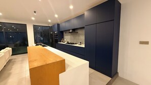 Cozinha moderna com bancada de madeira, armários escuros e painel decorativo geométrico.