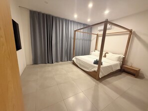Quarto com cama de dossel, mesa de cabeceira e televisão fixada na parede.