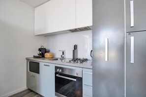 A compact kitchen with white cabinets, a stainless steel refrigerator, a built-in oven, and a coffee maker. - Top-Floor Apartment with Balcony - High Street (Prahran)