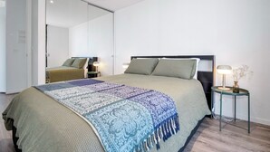 A modern bedroom with a large bed, a bedside table with a lamp, and a mirror on the wall. - Top-Floor Apartment with Balcony - High Street (Prahran)