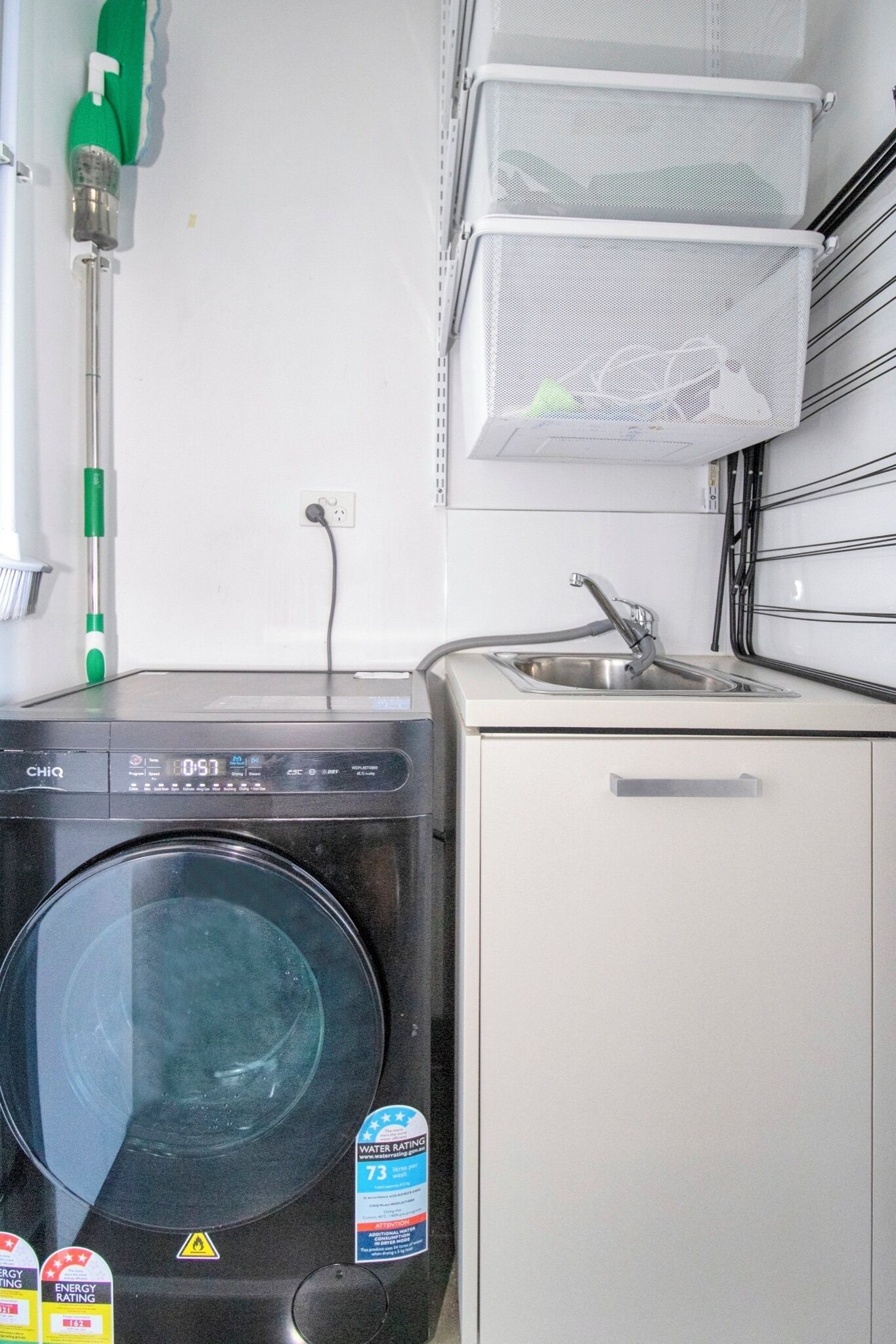 Una cocina compacta con lavadora, un lavabo y una escoba verde.