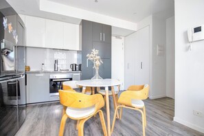A modern kitchen with grey cabinets, a stainless steel refrigerator, and a round dining table with wooden chairs. - Top-Floor Apartment with Balcony - High Street (Prahran)