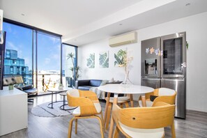 A modern living space with a dining area, kitchen, and large windows offering a city view. - Top-Floor Apartment with Balcony - High Street (Prahran)