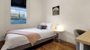 Een slaapkamer met een bed, een nachtkastje met een lamp, een stoel en uitzicht op een brug en water.