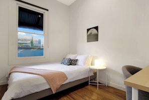 Ein Schlafzimmer mit Bett, Nachttisch mit Lampe, einem Sessel und Blick auf eine Brücke und Wasser vor dem Fenster.