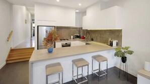 Een moderne keuken met een centraal eiland, barstoelen, een magnetron en een koelkast.