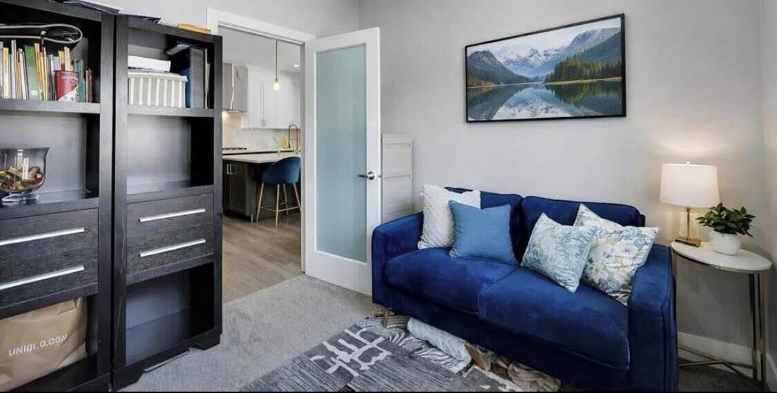 Une pièce avec un canapé bleu, une bibliothèque, un bureau et un tableau représentant un lac.