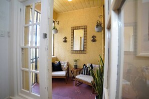 Ein Zimmer mit einer weißen Tür, einem Spiegel, einer Couch, einem Sessel und Topfpflanzen.