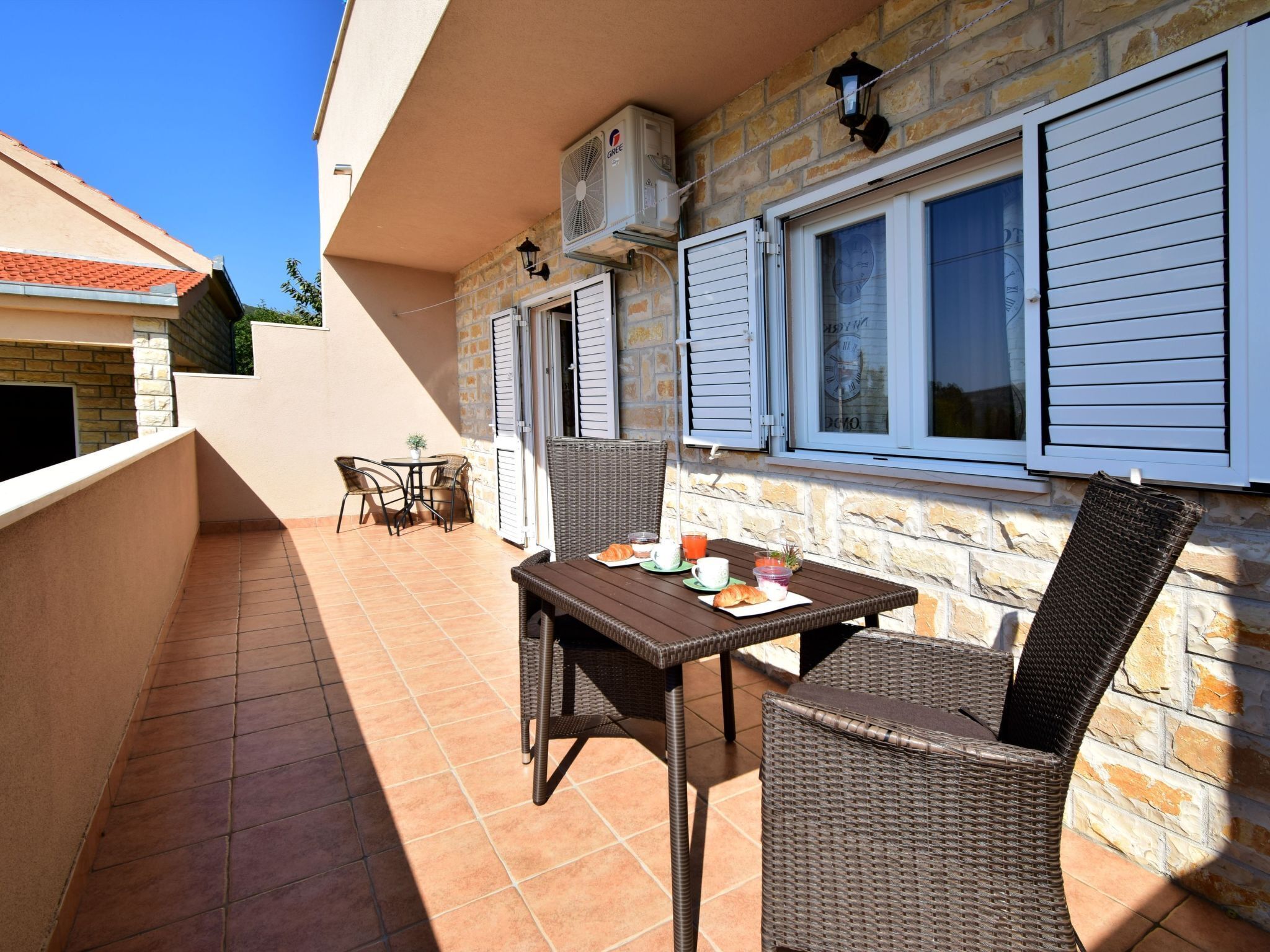 An outdoor patio with wicker furniture, a table set with a croissant, and a clock on the wall.