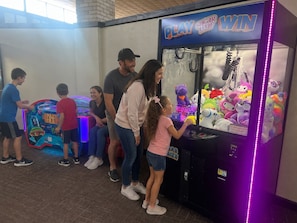 A family playing a claw machine game in a brightly lit indoor area with a visible arcade machine labeled 'PLAY SUGAR LOAF WIN'. - Charming 1-bedroom bed & breakfast in welcoming Oklahoma City (Oklahoma City)
