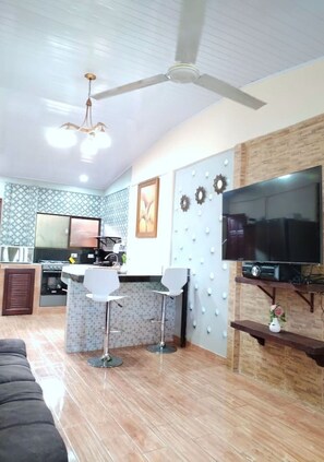 A modern kitchen with a built-in oven, a dining area with two white chairs, a large flat-screen TV, and a ceiling fan. - 2BR Home Near Ocotal Beach | 5 Min to the Beach, 8 Min to Coco (Coco)