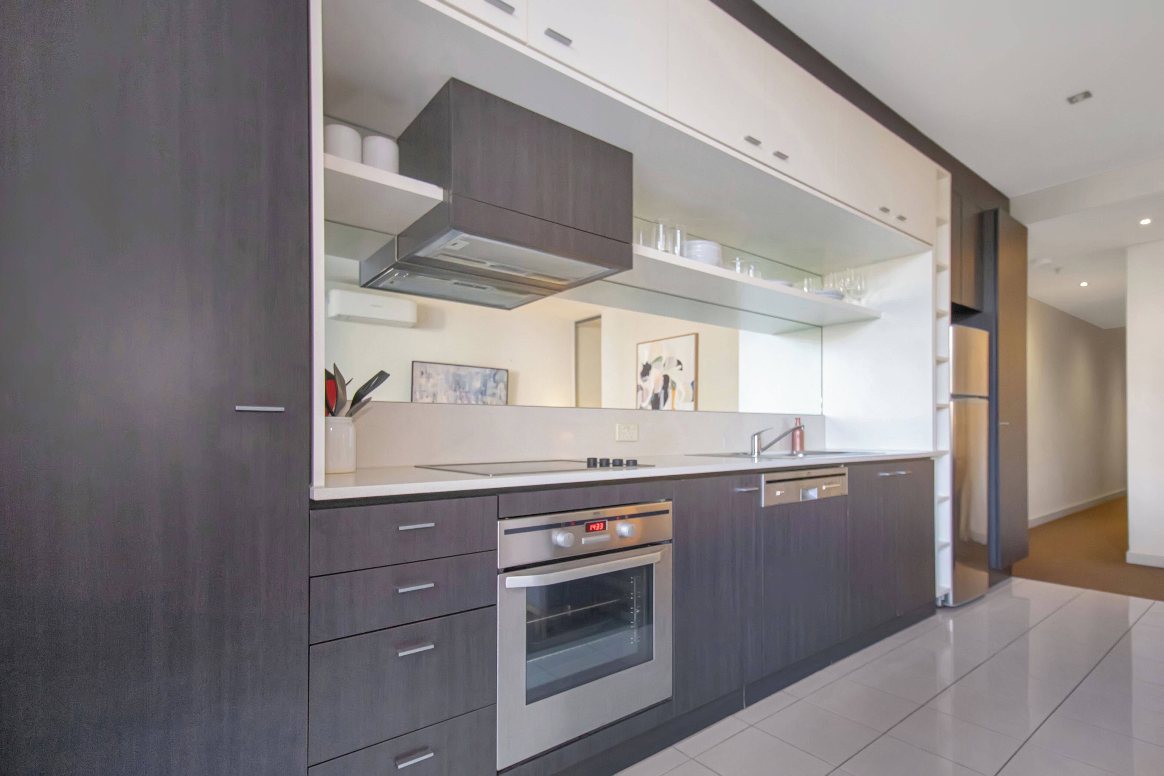 A modern kitchen with dark cabinetry, stainless steel appliances, and a large island with a built-in oven.