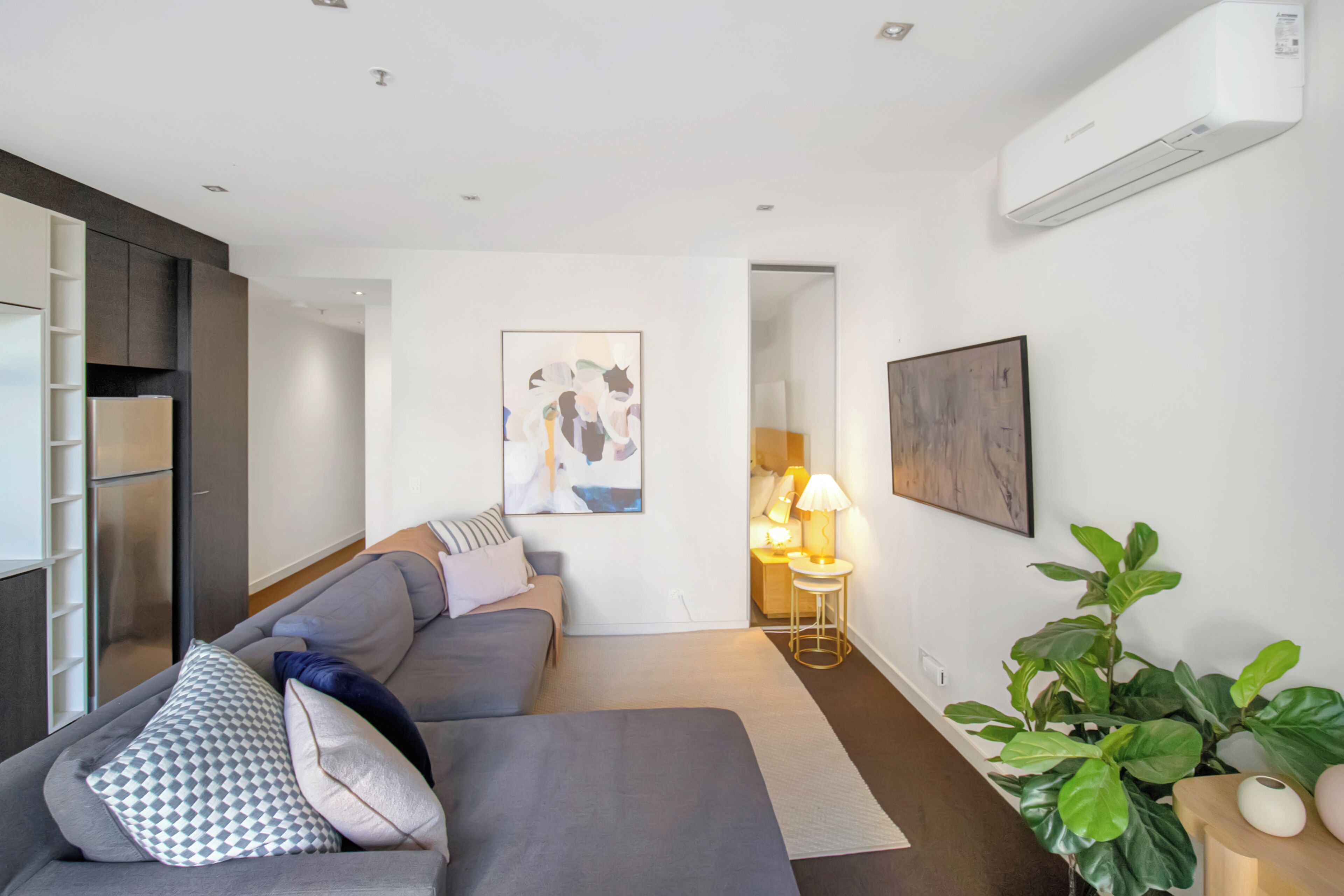 A modern living room with a sofa, a lamp, a painting, and a potted plant.