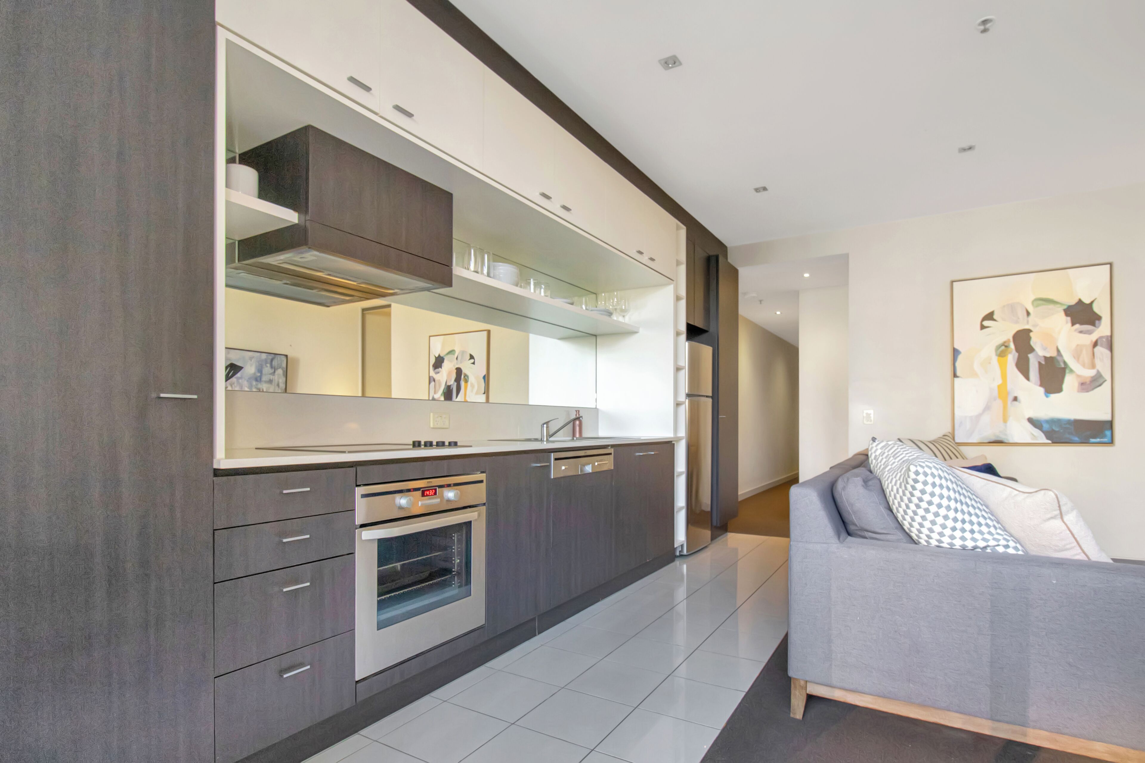 A modern kitchen with built-in appliances, a grey sofa, and a large mirror.