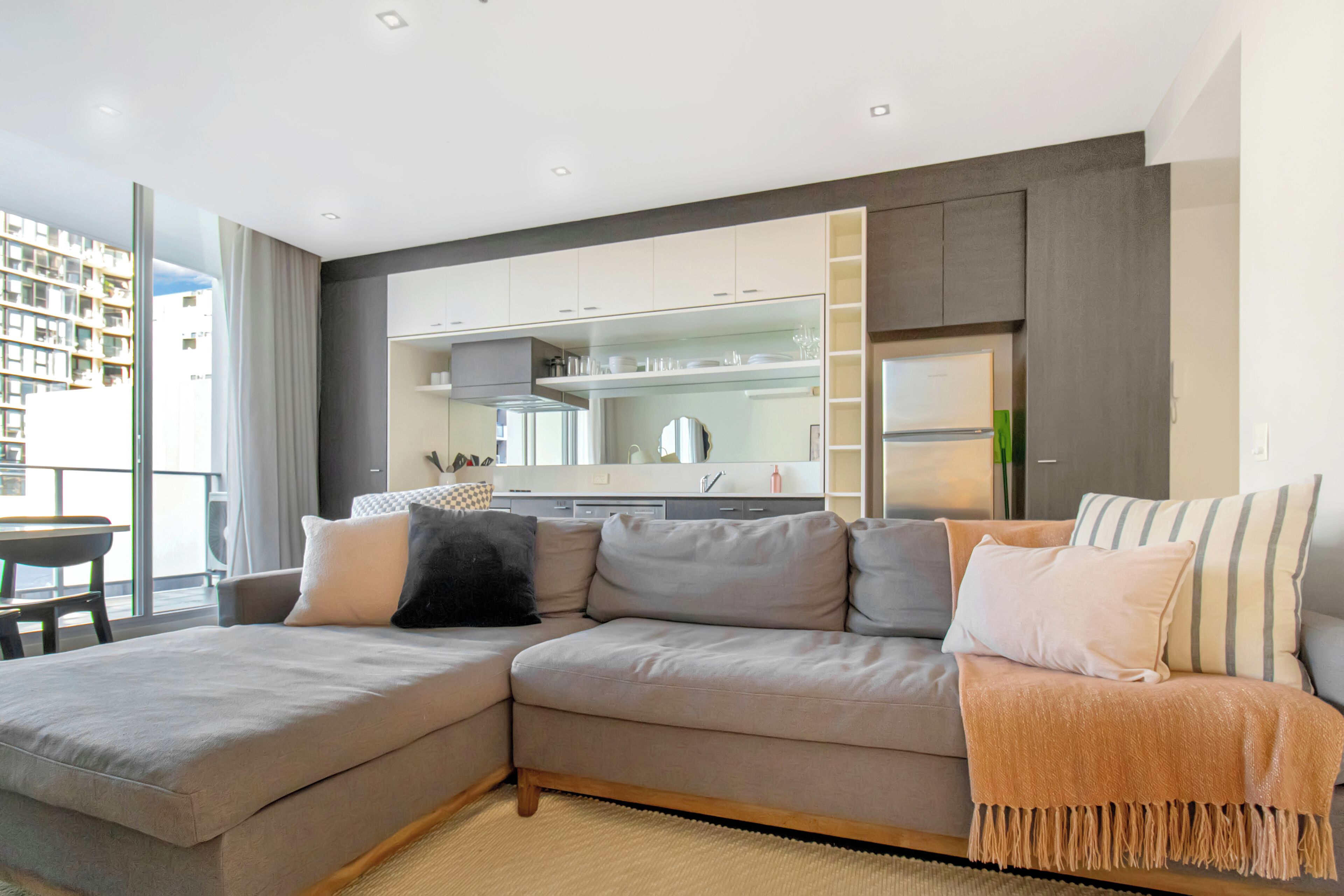 Una sala de estar moderna con un sofá seccional, una cocina con electrodomésticos integrados y un amplio ventanal con vistas a la ciudad.