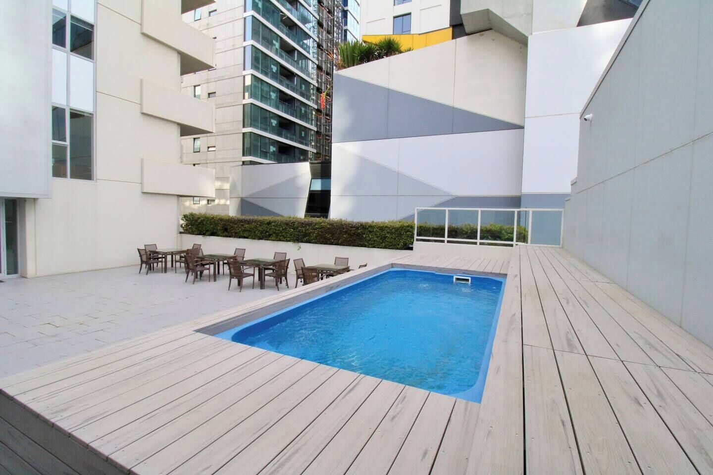 A rooftop pool with wooden decking, surrounded by modern buildings.