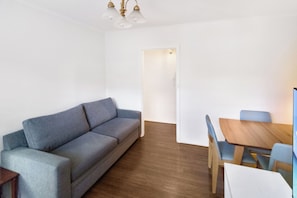 A room with a grey sofa, a wooden dining table with blue chairs, and a wooden floor. - Park Street Apartment - St Kilda West (Saint Kilda West)