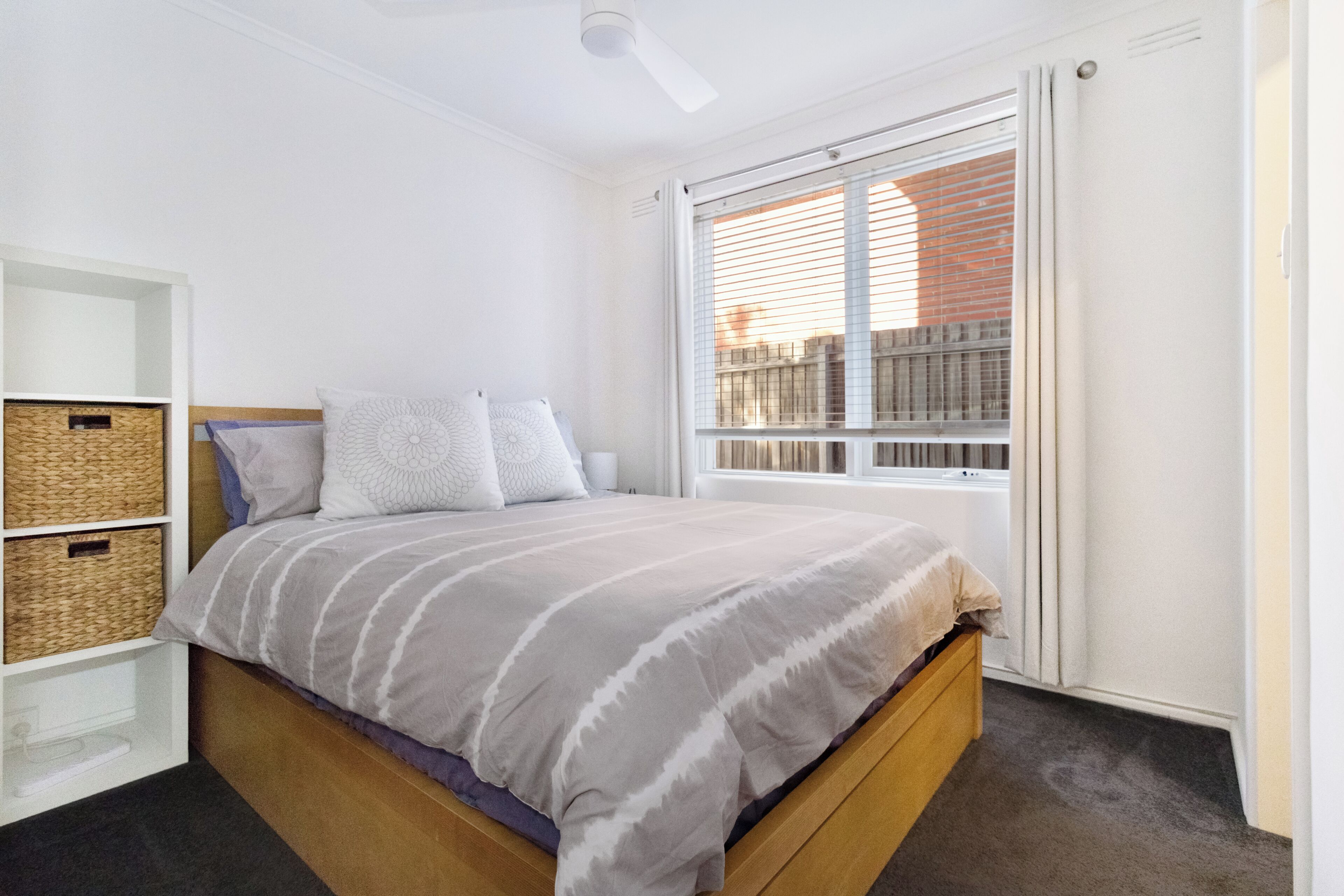 Une chambre à coucher avec un lit, une fenêtre et une étagère intégrée avec des paniers.