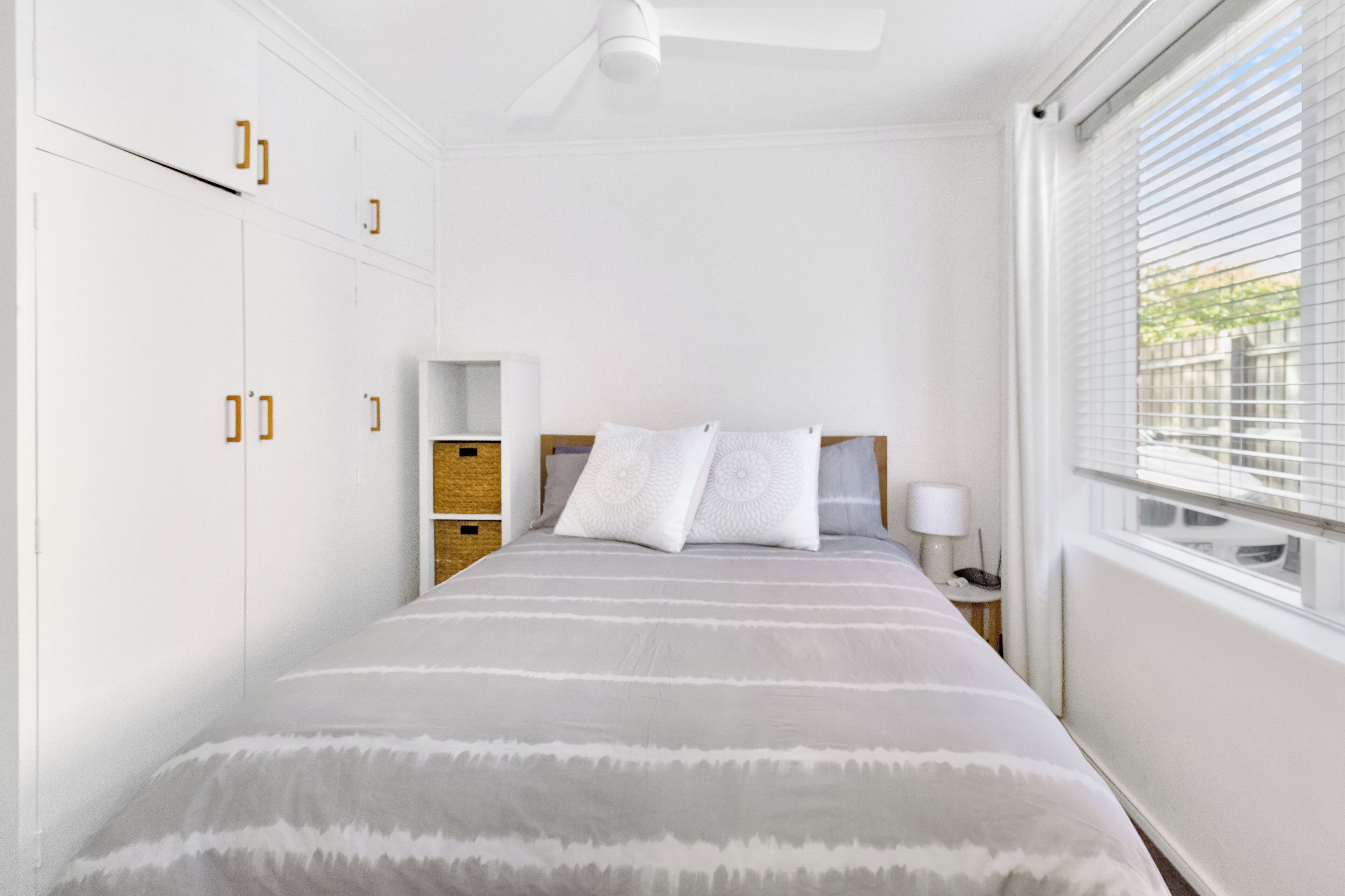 A bedroom with a bed, a nightstand, a lamp, and a window with blinds.