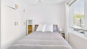 Ein Schlafzimmer mit Bett, Nachttisch, Lampe und einem Fenster mit Jalousien.