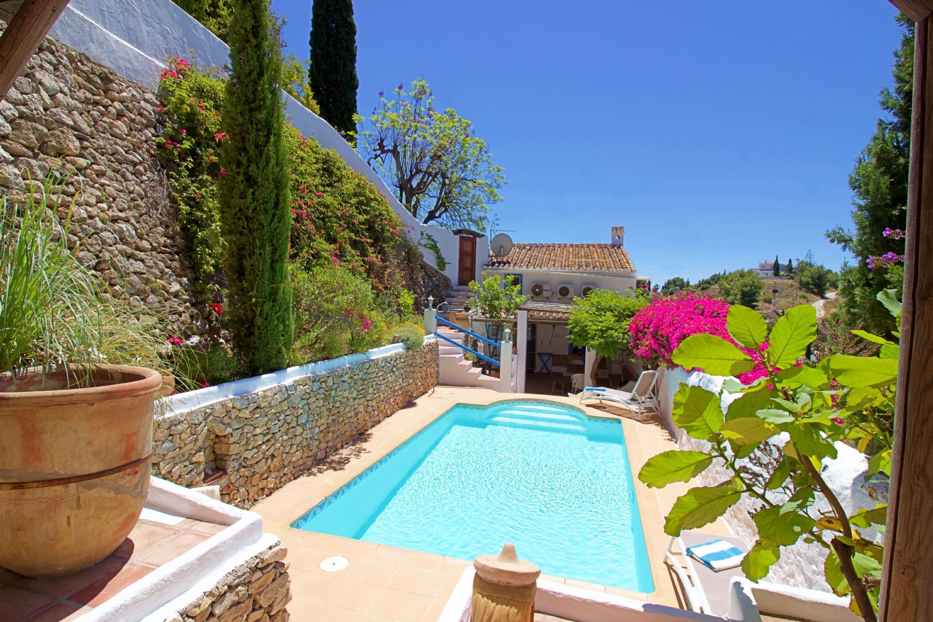 A pool area with a stone wall, a wooden deck, and a building in the background.