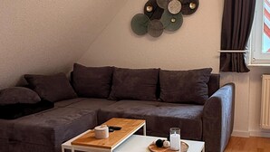 Uma sala de estar aconchegante com um sofá seccional, uma mesa de centro e uma peça decorativa na parede.