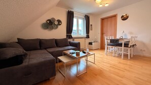 Uma sala de estar moderna com um sofá seccional, uma mesa de centro, uma mesa de jantar com cadeiras, uma janela com cortinas e um lustre fixado na parede.