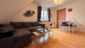 Una sala de estar moderna con un sofá seccional, una mesa de centro, una mesa de comedor con sillas, una ventana con cortinas y una lámpara de pared.