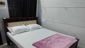 Una cama individual con cabecera de madera, ropa de cama blanca y una manta rosa.