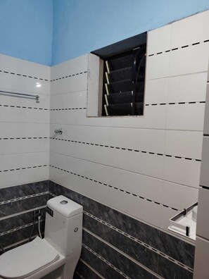 Une salle de bain avec des murs recouverts de carreaux blancs, un mur d’accent en marbre noir, des toilettes, un espace douche et une fenêtre à cadre noir.