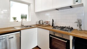 A modern kitchen with white cabinets, a dishwasher, a stove, and a window with plants. - Beachfront Marine Parade - Rooftop BBQ - Luna Park (Saint Kilda, Victoria, AU)