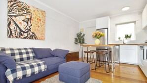 A modern living room with a sofa, ottoman, and a painting on the wall. - Beachfront Marine Parade - Rooftop BBQ - Luna Park (Saint Kilda, Victoria, AU)