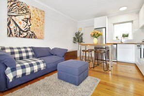 A modern living room with a sofa, ottoman, and a painting on the wall. - Beachfront Marine Parade - Rooftop BBQ - Luna Park (Saint Kilda, Victoria, AU)