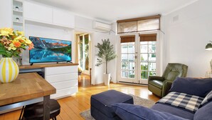 A modern living room with a flat-screen TV, a dining table, a sofa, and a green chair. - Beachfront Marine Parade - Rooftop BBQ - Luna Park (Saint Kilda, Victoria, AU)