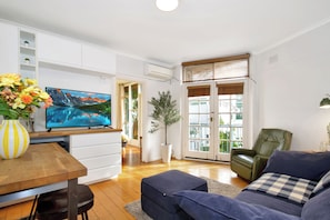A modern living room with a flat-screen TV, a dining table, a sofa, and a green chair. - Beachfront Marine Parade - Rooftop BBQ - Luna Park (Saint Kilda, Victoria, AU)