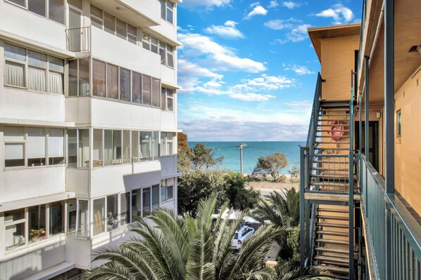 A multi-story building with balconies, a staircase, and a view of the sea. - Beachfront Marine Parade - Rooftop BBQ - Luna Park (Saint Kilda, Victoria, AU)