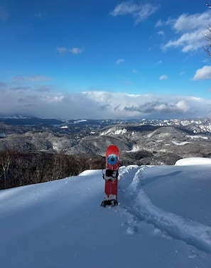 Ein Snowboard auf einem verschneiten Hang mit einer bergigen Landschaft im Hintergrund.