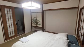 A traditional Japanese-style bedroom with a wooden ceiling, a bed with white and blue bedding, and a sliding door leading to a bathroom.