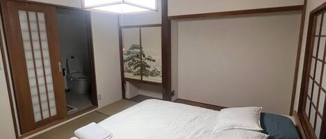 A traditional Japanese-style bedroom with a wooden ceiling, a bed with white and blue bedding, and a sliding door leading to a bathroom.