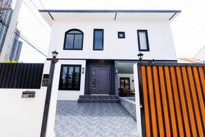 Ein modernes, zweistöckiges Haus mit einer dunklen Haustür, einer kleinen Veranda und einem befestigten Eingangsbereich.