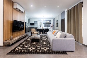 A modern living room with a grey sofa, a coffee table, and a TV mounted on the wall. - Acadia 5BR (Banglamung)