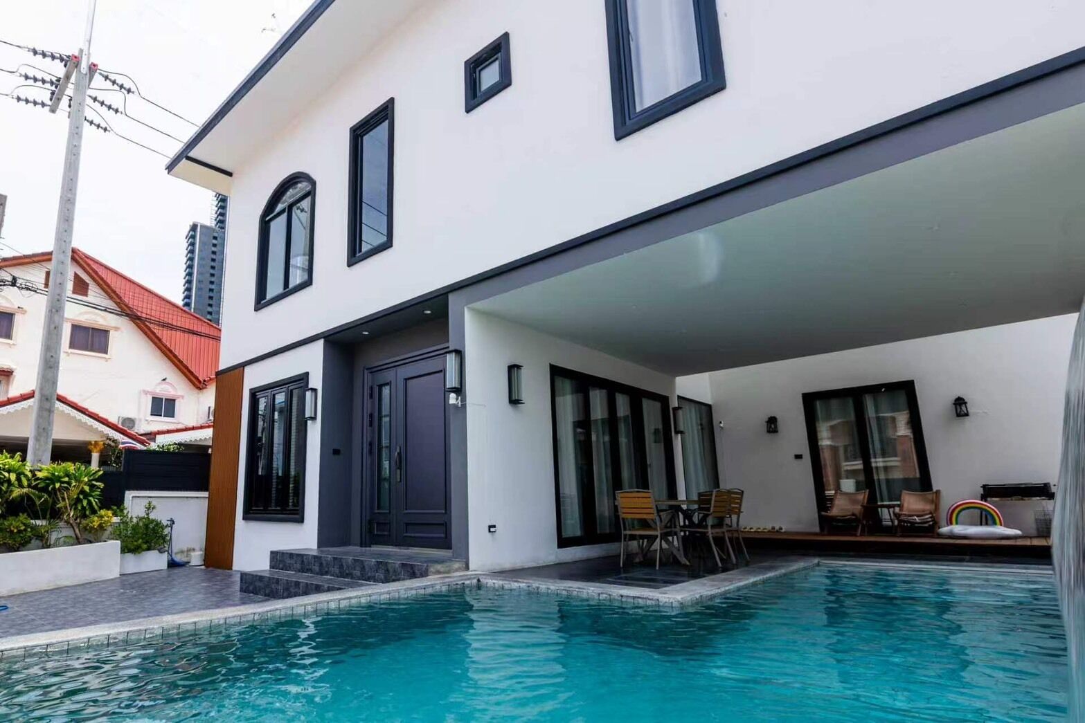 A modern two-story house with a swimming pool, a covered patio, and a dining area.